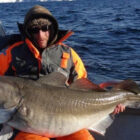 Angler sat on a boat on a fjord holding a large cod