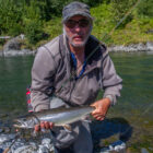 Man knelt in a river in Alaska holding a dolly varden fish