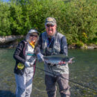 Lady and man standing in a river in Alaska, the man holding a pink salmon