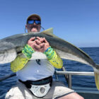 Angler sitting on a boat holding a large kingfish