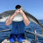 Angler sitting on a boat holding a large kingfish