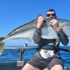 Angler sitting on a boat at sea holding a yellow fin kingfish