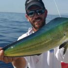 Angler holding a mahi mahi fish on a boat in open ocean