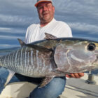 Angler holding a large tuna fish on a boat in open ocean