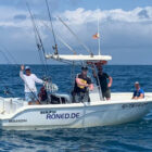 Fishing charter boat with rods mounted and four anglers aboard