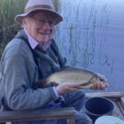 Angler sat on a seat beside a lake in Sweden holding a ide fish