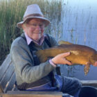 Angler sat on a seat beside a lake holding a tench