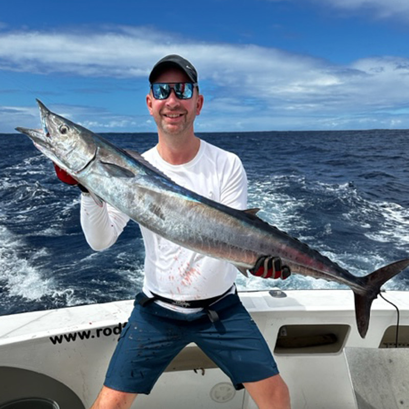 Angler stood on a boat holding a wahoo fish