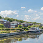 A motorboat docked in front of a row of brick holiday homes lined with green trees.