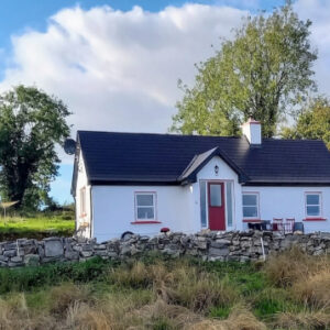 Front view of a white traditional Irish cottage with a red door behind a low stone wall.