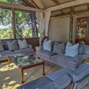 An indoor lounge area inside a luxury safari tent with grey sofas, patterned pillows, and a glass-top coffee table.