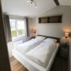 Cosy bedroom inside a chalet featuring a double bed with white duvets, bedside tables, and wall lamps.