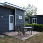 Patio area with a table and four chairs outside a dark siding chalet on a checked tiled floor.