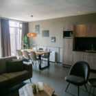 Open-concept bungalow interior featuring a dark sofa, dining table, dark grey tile floors, and wood cabinetry.