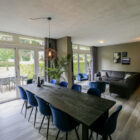 Spacious dining and living area with a long black table, blue chairs, dark sectional sofa, and full-length glass doors.
