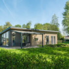 Exterior view of a modern wood-clad lodge with large glass windows and an outdoor seating area on a green lawn.