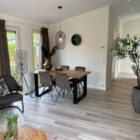 Modern dining area with a wooden table, brown chairs, light wood flooring, and large houseplant.