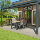 Outdoor covered patio of a wooden lodge with a patio dining set next to a lawn and pond.