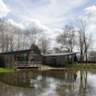 Modern wooden chalets with sloped roofs reflected in a calm body of water under a cloudy sky.