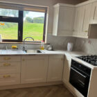 Modern white fitted kitchen with integrated oven, gas hob, and a scenic window view.