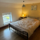 Bright bedroom with a double bed, warm yellow accent wall, and wood flooring.