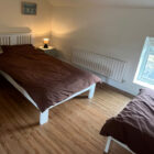 Twin bedroom featuring two single beds with dark brown duvets and light wood floors.
