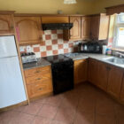 Traditional wooden kitchen with tiled splashback, white refrigerator, and black stove.