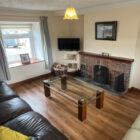 Living area with a glass coffee table, leather sofas, and a brick fireplace.