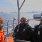 Passengers wearing protective warm gear riding on an open boat on the sea.