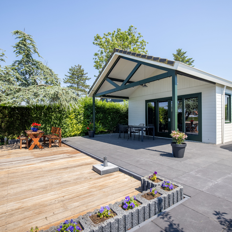 Modern chalet with a covered patio, outdoor dining set, timber deck, and stone flower beds.