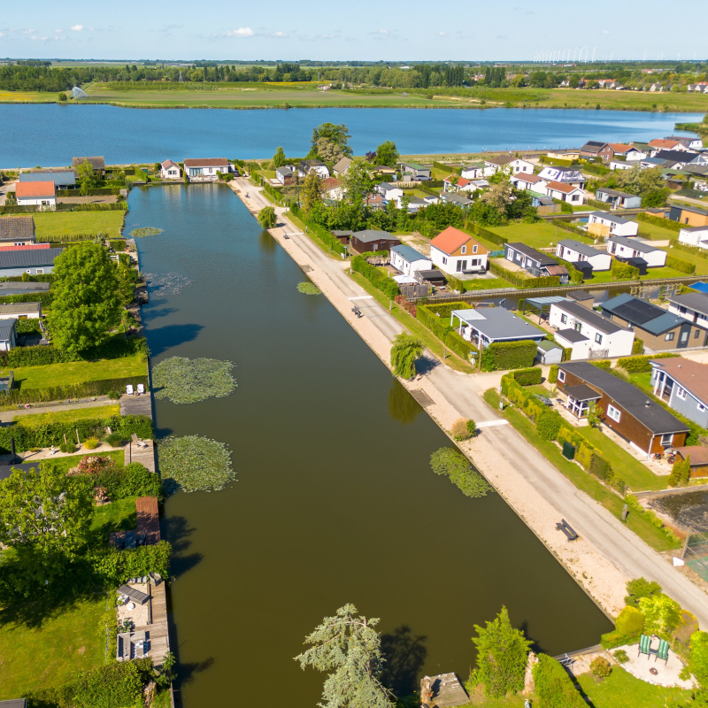 Aerial view of a long fishing canal lined with holiday homes, leading out toward a large lake.