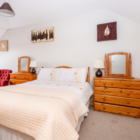 Cosy bedroom with a double bed, pine wooden chest of drawers, vanity mirrors, and neutral decor.