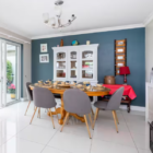 Bright dining room with a blue accent wall, large wooden table, grey mid-century chairs, and a white hutch cabinet.